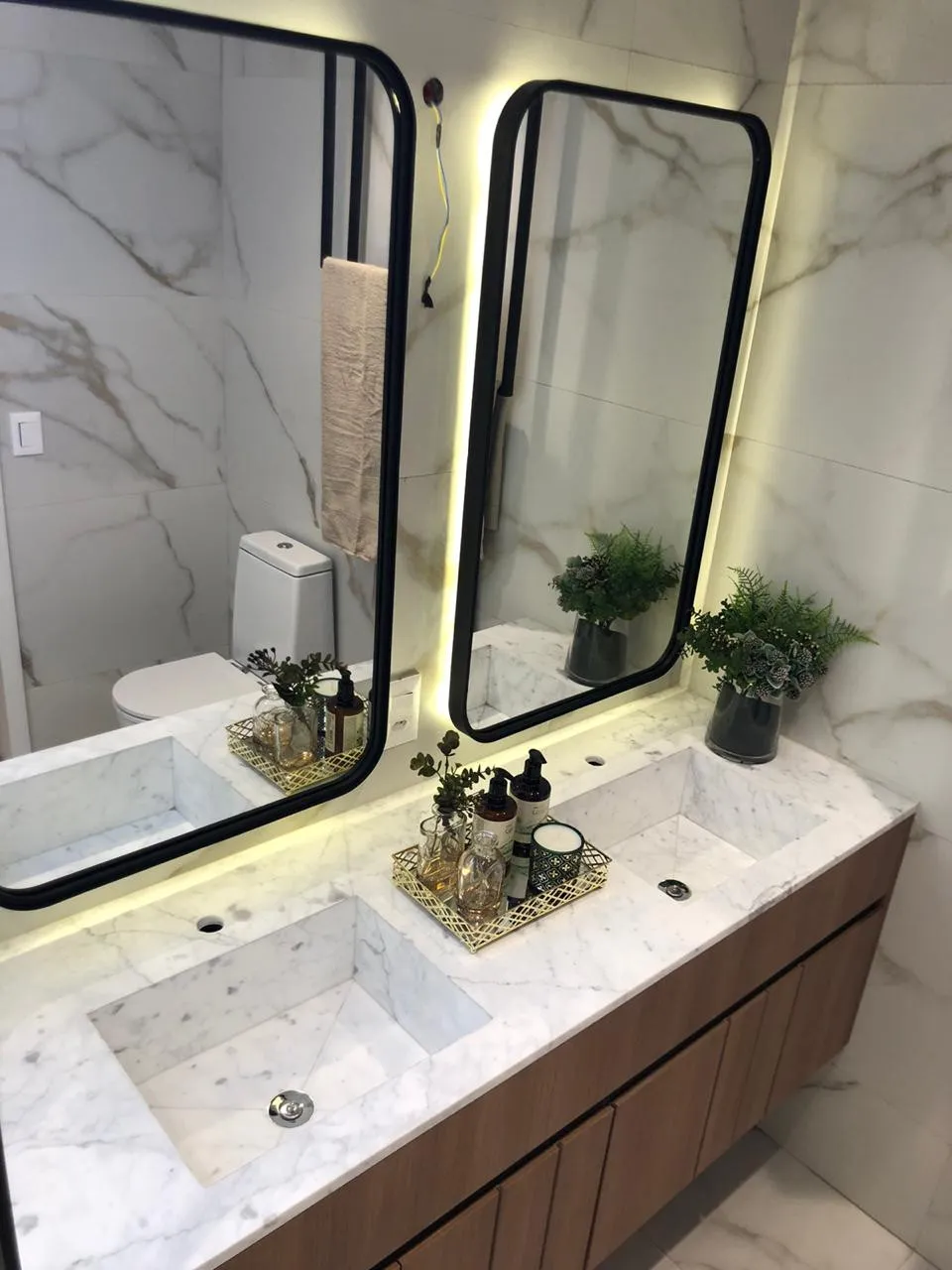 Bancada de mármore branco com cuba esculpida no próprio material, sob espelhos iluminados