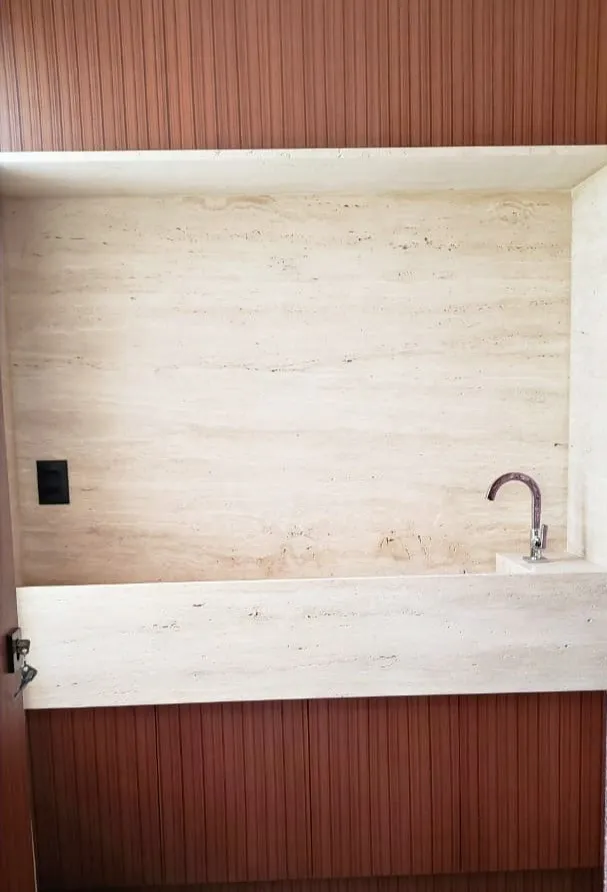 Bancada suspensa de travertino em lavabo com parede ripada de madeira
