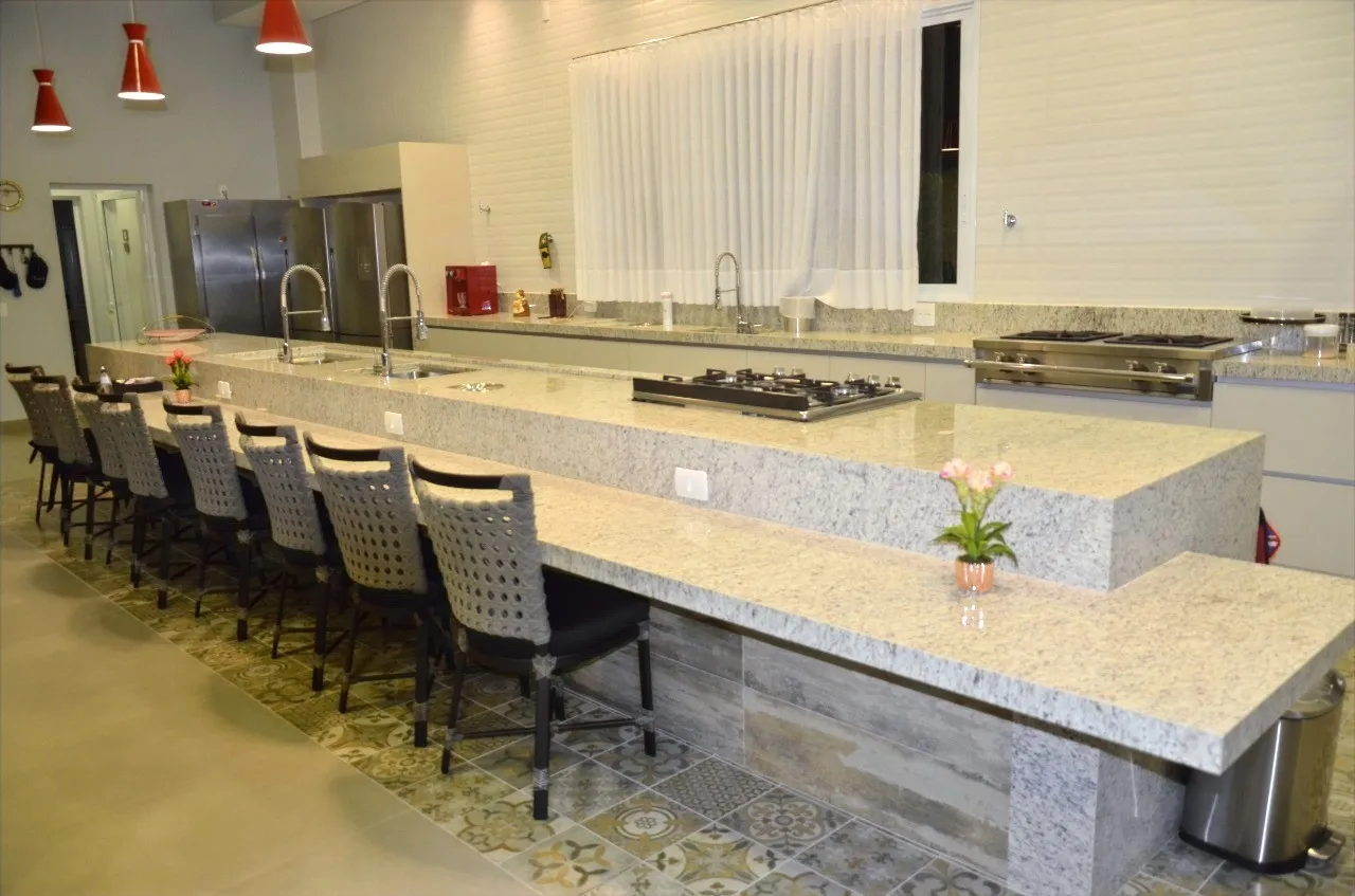 Bancada comprida de granito claro com bordas engrossadas, servindo de balcão para banquetas altas