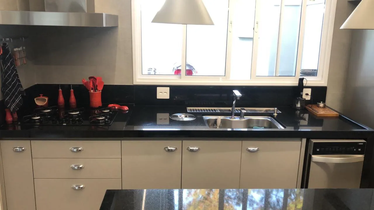 Bancada de granito preto com cuba dupla e cooktop, sob janela de cozinha