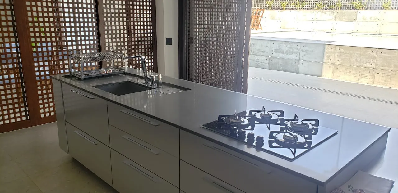 Ilha de cozinha com tampo de pedra cinza claro e cooktop, diante de painel vazado