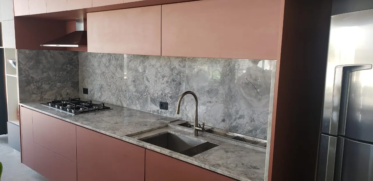 Bancada e frontão de mármore acinzentado em cozinha com armários terracota