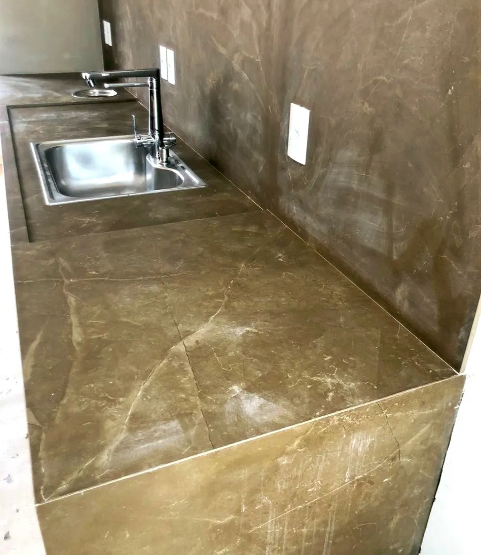 Bancada de mármore marrom com cuba de inox embutida e lateral engrossada, ainda em obra
