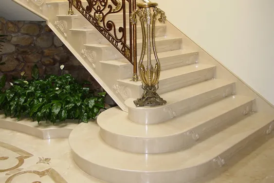 Escada curva de mármore claro com corrimão de ferro trabalhado, ao lado de parede de pedra e jardim